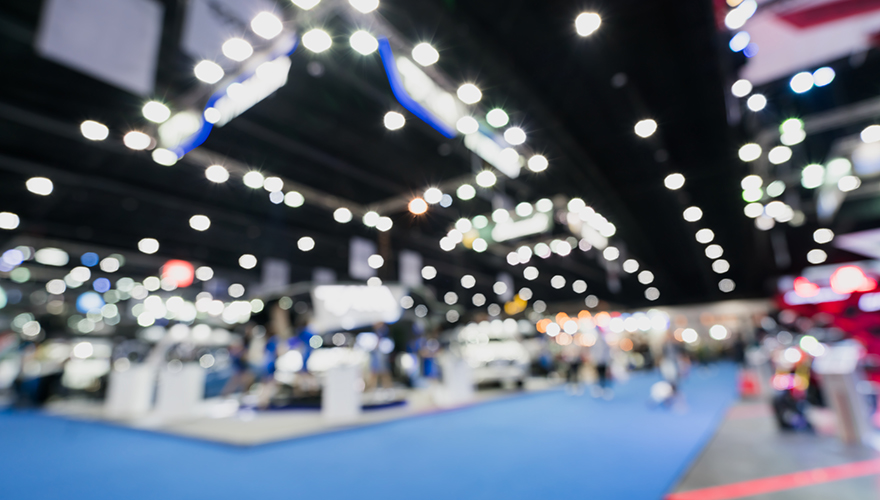Blurred, defocused background of public event exhibition hall showing cars and automobiles, business commercial event concept