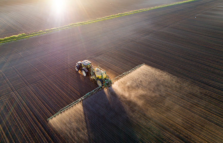 Aerial image of tractor spraying soil and young crop in springtime in field; Shutterstock ID 1084410071; Purchase Order: -